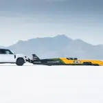 水素エンジンを搭載し「世界最高速」を記録したJCB「ハイドロマックス」を押し出すランドローバー・ディフェンダー・オクタ